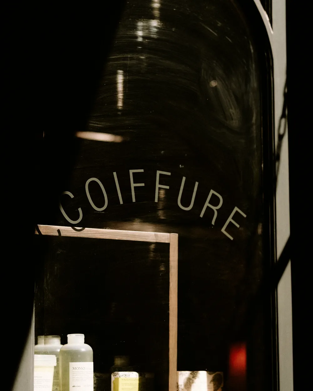 Vitrine d'un salon de coiffure le soir, avec les produits en devanture